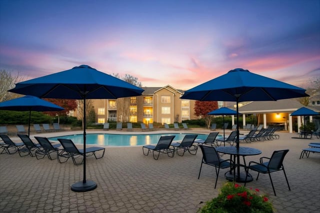 Resort-style swimming pool with lounge chairs and umbrellas at dusk.
