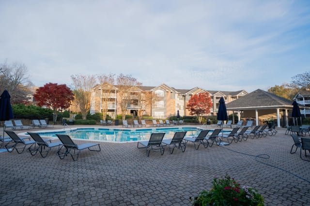 Resort-style swimming pool with lounge chairs and a cabana area at an apartment complex.