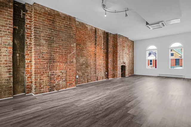 Unfurnished apartment living room with exposed brick wall and hardwood floors.