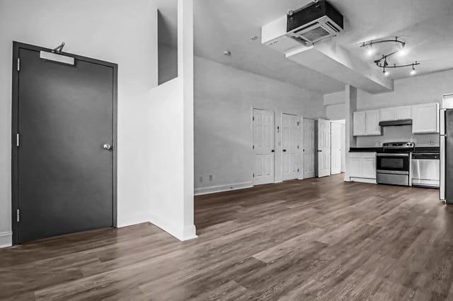 Interior view of a kitchen and living area with hardwood floors and white cabinets.