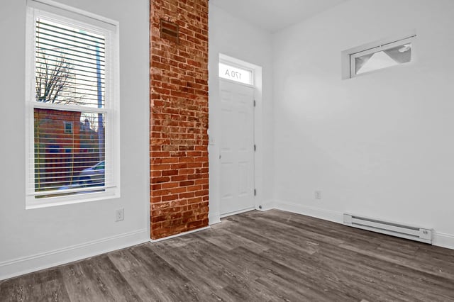 Interior view of an apartment with exposed brick, window, and door.