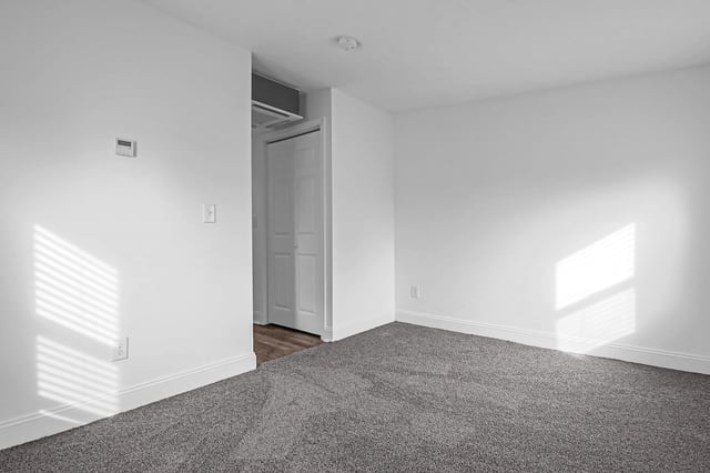 Empty apartment bedroom with gray carpet, white walls, and a closet.