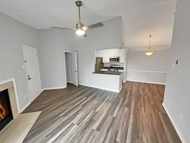 Living room with fireplace, ceiling fan, and open kitchen with stainless steel appliances.