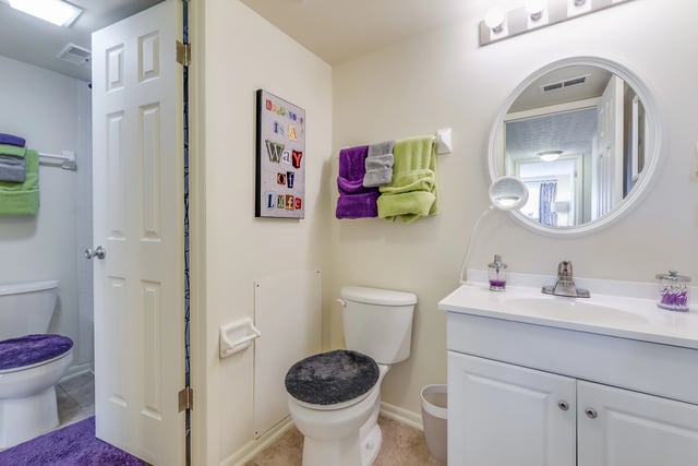 Bathroom vanity with sink and round mirror above, toilet and shower visible through doorway.