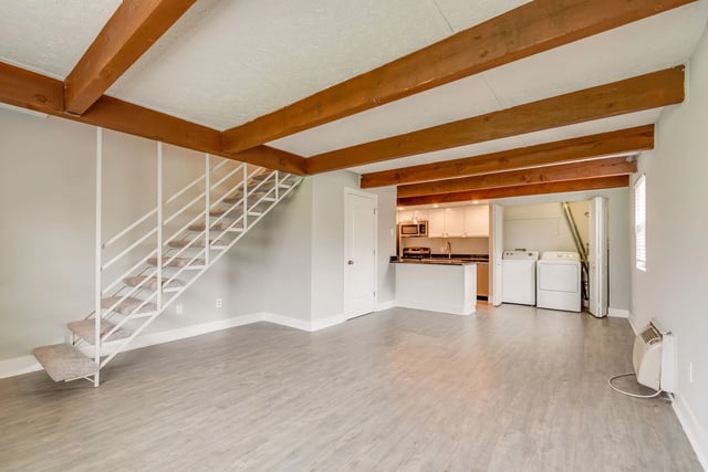 Open-concept living area with stairs leading to upper level, full kitchen with white cabinets and granite countertops, and in-unit washer and dryer.
