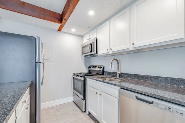 Modern kitchen with stainless steel appliances, white cabinets, granite countertops, and a wooden beam ceiling.