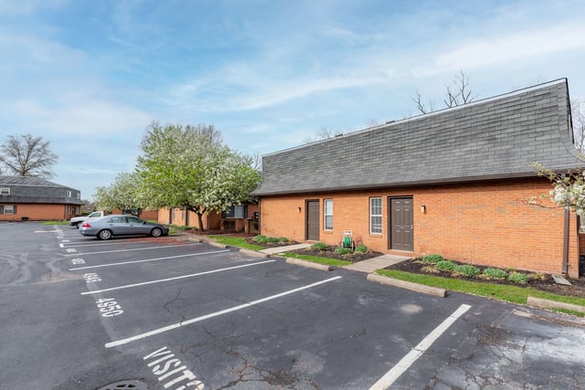 Exterior view of brick apartment buildings with parking lot and landscaping.