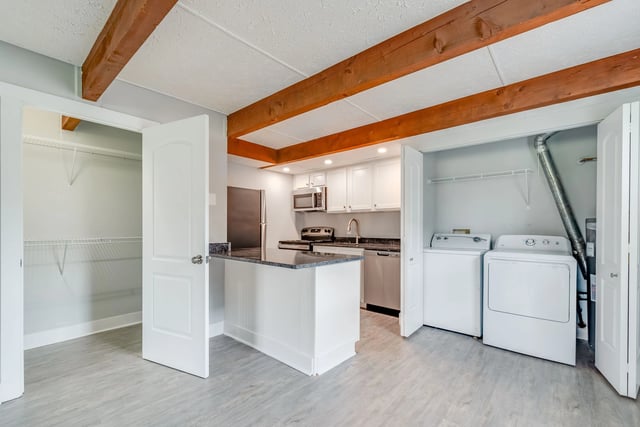 Kitchen with granite countertop, white cabinets, stainless steel appliances, and stacked washer and dryer.