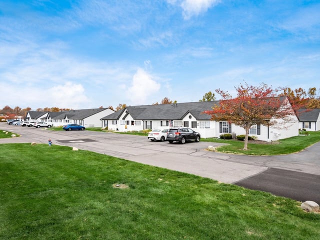 Exterior view of apartment buildings with manicured lawns and parked cars.