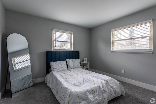 Modern bedroom with a queen-size bed, large mirror, and grey carpet.