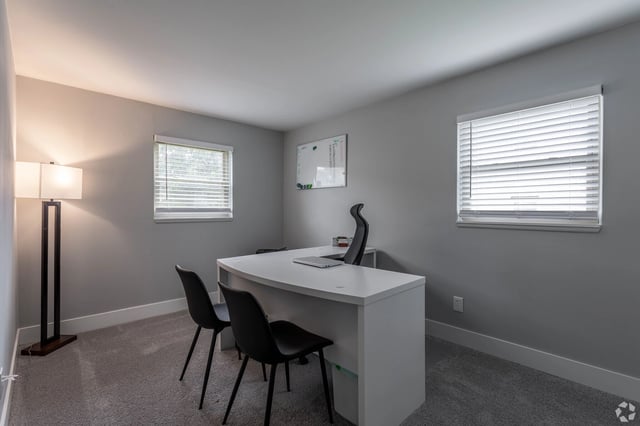 Modern home office with white desk, black chairs, and floor lamp.