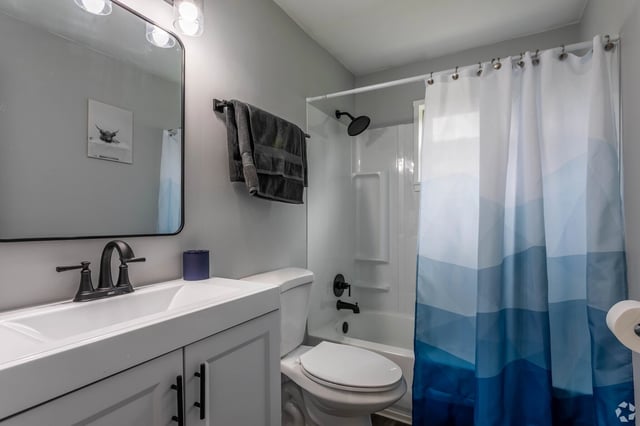 Modern bathroom with a white vanity, black faucet, and a bathtub with a blue gradient shower curtain.