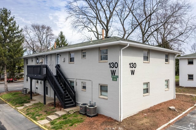 Exterior of a two-story apartment building with light gray brick, black stairs, and trees.