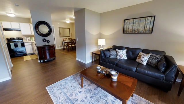 Spacious living room with black leather sofa, coffee table, dining area, and kitchen.