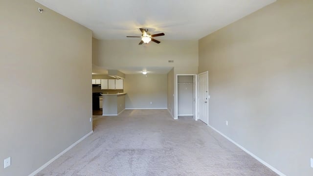 Interior view of a spacious living room with a ceiling fan, leading to an open kitchen area and a closet near the entrance.