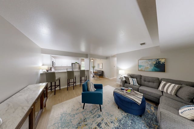 Living room and kitchen area with gray sectional sofa, blue armchair, bar seating, and modern finishes.