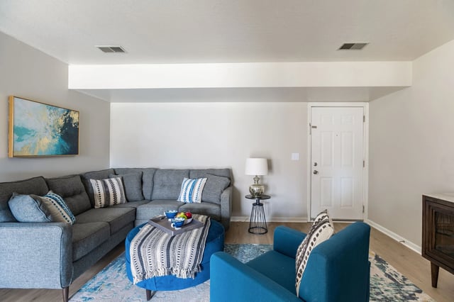 Modern living room with sectional sofa, blue armchair, ottoman, and abstract art.