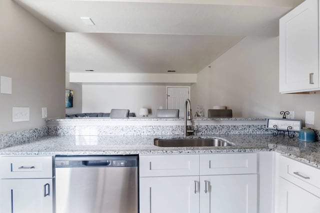 Kitchen with granite countertops, stainless steel dishwasher, and white cabinetry.