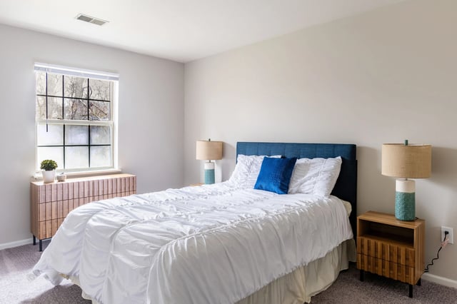 Cozy bedroom with a queen-size bed, white linens, blue accents, and a window view.