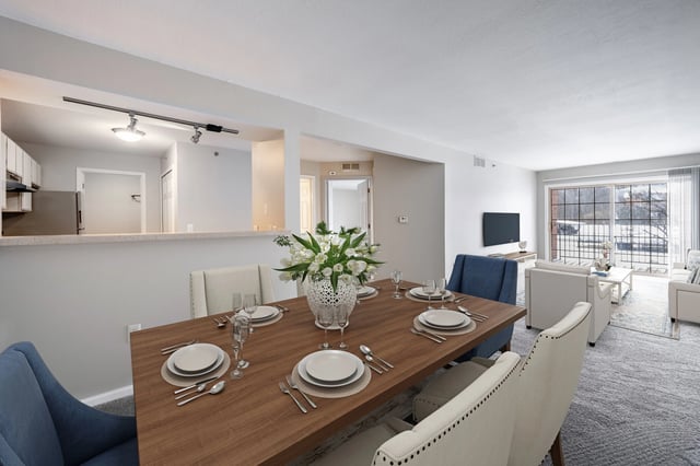 Dining room with a table set for six people, a kitchen area, and a living room visible.