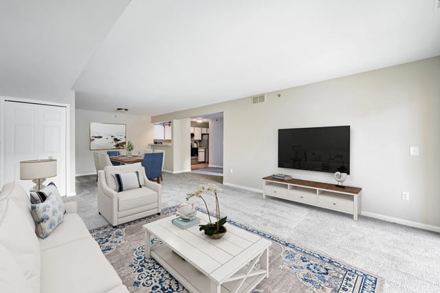 Living room and dining area of an apartment with white furniture and a large TV.