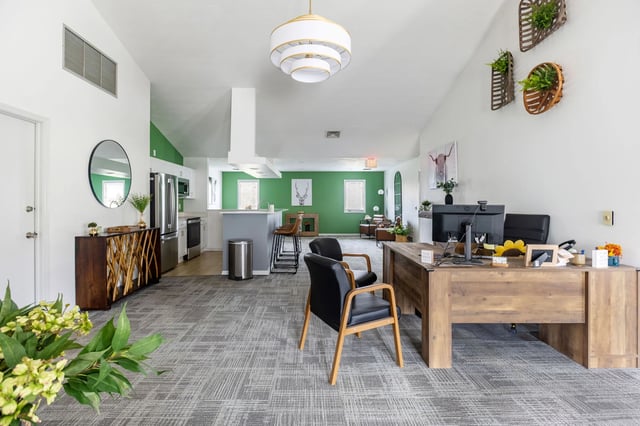 Modern reception area with a large desk, chairs, and a kitchenette in the background.