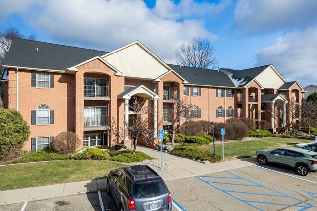 Exterior view of a brick apartment building with balconies and parked cars.
