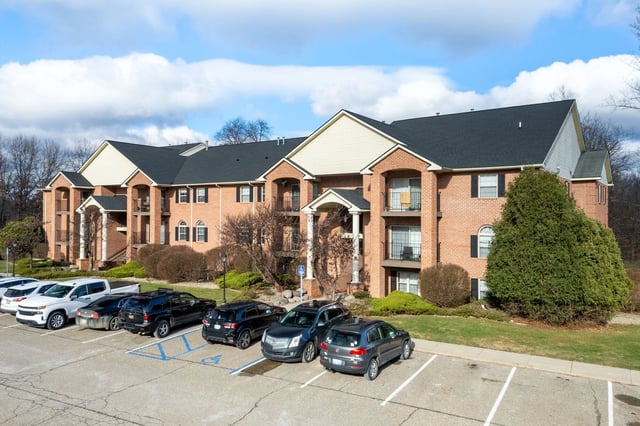 Exterior view of a brick apartment building with a parking lot in front.