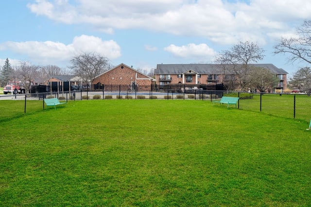 Lush green lawn with benches and a fenced swimming pool area in the background.