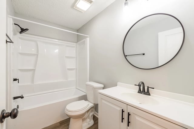Modern bathroom with white vanity, round mirror, and white bathtub with shower.