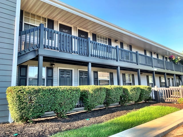 Exterior view of apartment buildings with balconies and neatly trimmed hedges.
