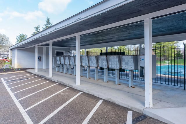 Mailboxes next to a covered parking area with a pool in the background.