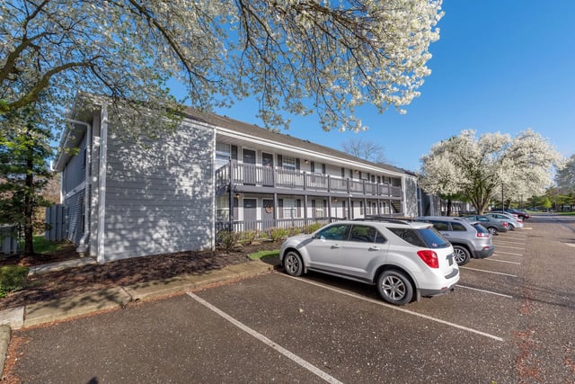 Exterior of an apartment building with a parking lot and blooming trees.