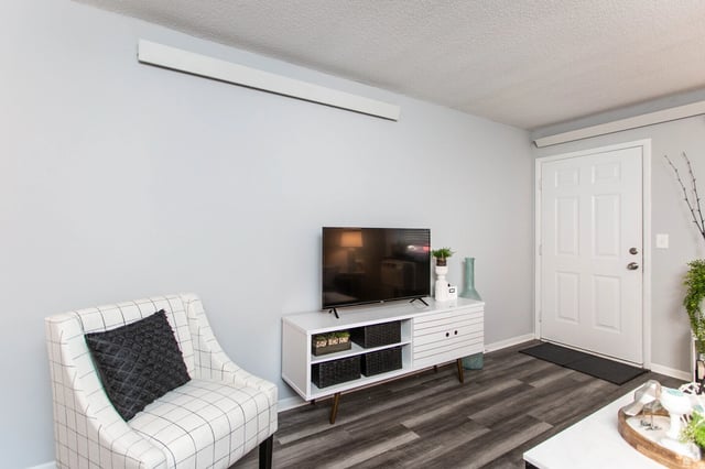 A modern living room with a plaid armchair, a white media console with a TV, and a white front door.