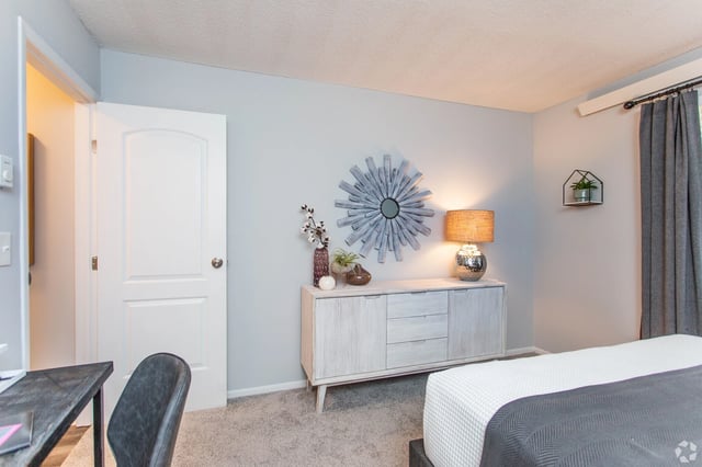 Bedroom with a white dresser, mirror, lamp, and a bed with gray and white bedding.