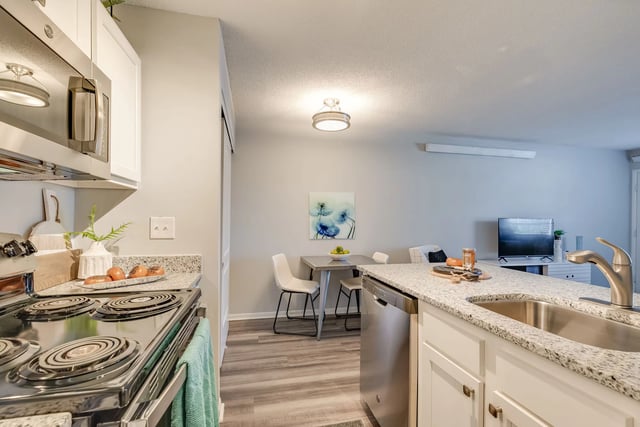 Modern kitchen with stainless steel appliances and granite countertops, open to dining and living area.