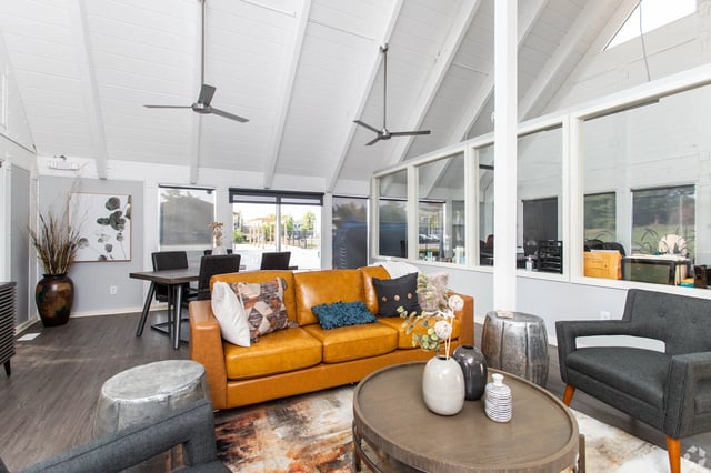 Interior of a community lounge area with a tan leather sofa, dark gray accent chairs, and a coffee table.