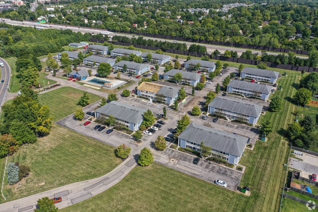 Aerial view of a multifamily apartment complex with multiple buildings, a pool, and surrounding greenery.