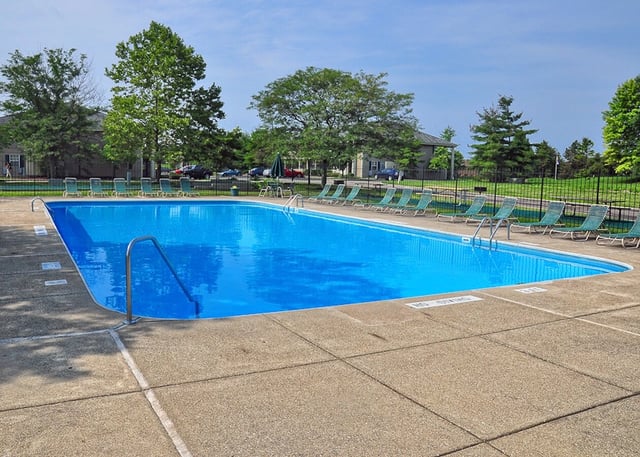 Outdoor swimming pool with lounge chairs and trees in the background.