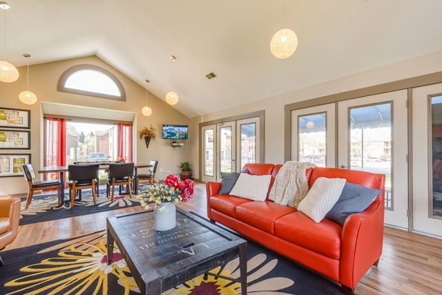 Community lounge area with orange sofa, coffee table, dining table, chairs, and TV.