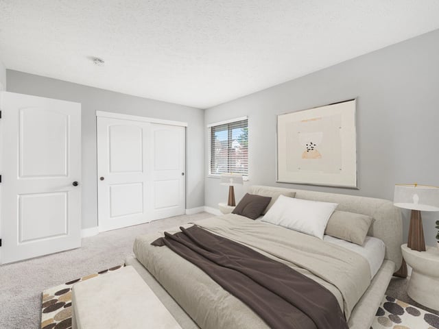 A modern bedroom with a king-size bed, sliding closet doors, and a large framed picture on the wall.