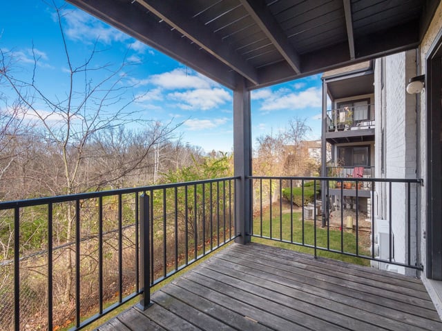 View from a balcony overlooking trees and a courtyard with apartment buildings in the background.