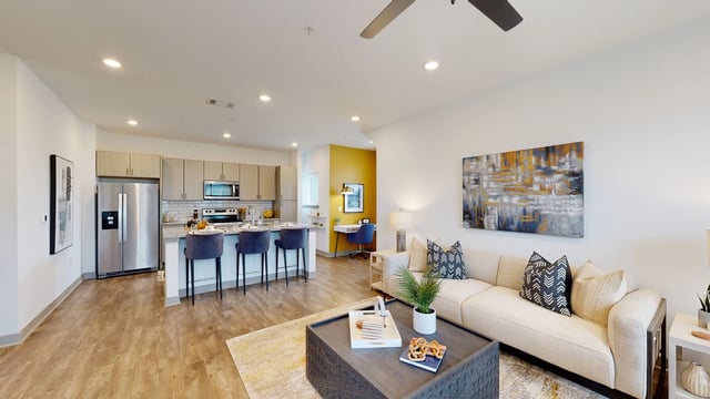 Open-concept living room and kitchen with modern finishes, island seating, and a couch.