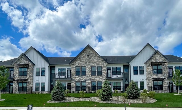 Exterior of a modern apartment building with stone and white siding, balconies, and manicured landscaping under a cloudy sky.