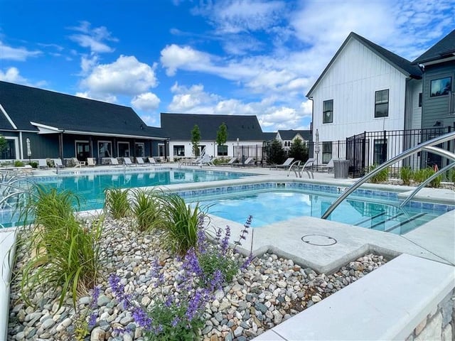 Outdoor swimming pool and spa with lounge chairs and buildings in the background.