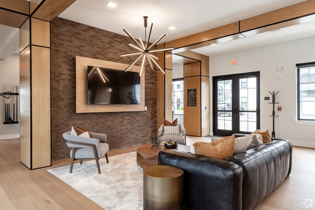 Lounge area with leather couch, armchairs, coffee table, and TV mounted on brick wall.