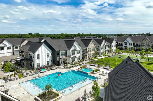 Aerial view of a modern apartment complex featuring a large outdoor swimming pool and surrounding green spaces.
