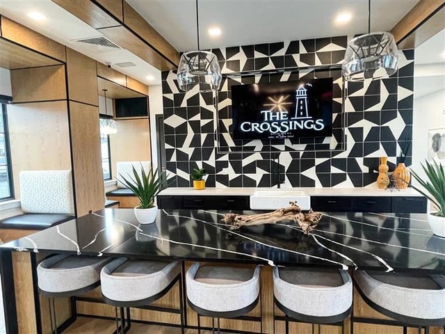 The Crossings apartment logo displayed on a TV screen above a modern counter with bar stools.