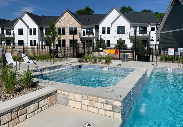 Apartment complex outdoor swimming pool and hot tub area with lounge chairs.