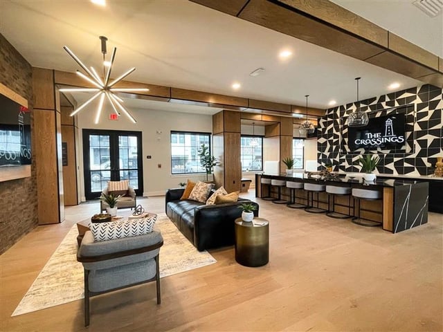 Modern lounge area with black leather sofa, decorative chandelier, and a bar with stools.